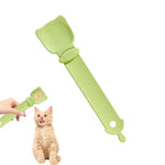 Load image into Gallery viewer, Green cat-shaped strip feeder spoon being squeezed to dispense wet food for a licking cat sitting nearby