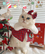 Load image into Gallery viewer, Cat wearing a red plaid Christmas shawl cloak with white fur trim, bell, and matching bow hairpin indoors near holiday decor