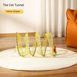 Load image into Gallery viewer, Folded S shape yellow striped cat tunnel toy with attached mouse and feather on round white rug indoors