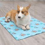 Load image into Gallery viewer, Corgi dog resting on a blue cooling dog mat with ice gel and winter-themed patterns on a wooden floor.