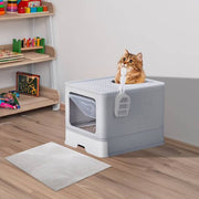 Grey enclosed cat litter box with slide-out tray and top-exit design, featuring a cat sitting on top and a scoop attached.