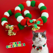 Christmas pet collar with red, green, and white plush balls, bow, and bells, worn by a cat on a red background