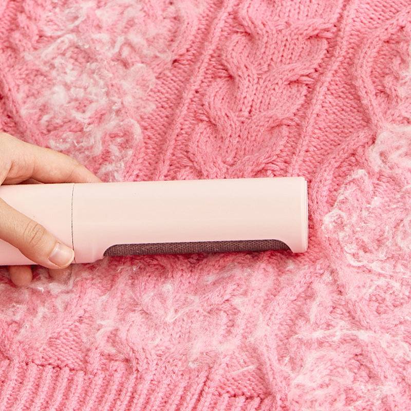 Pink 2-in-1 Pet Hair Remover Brush cleaning pet fur from a pink knitted sweater. Reusable and eco-friendly lint roller for home use.