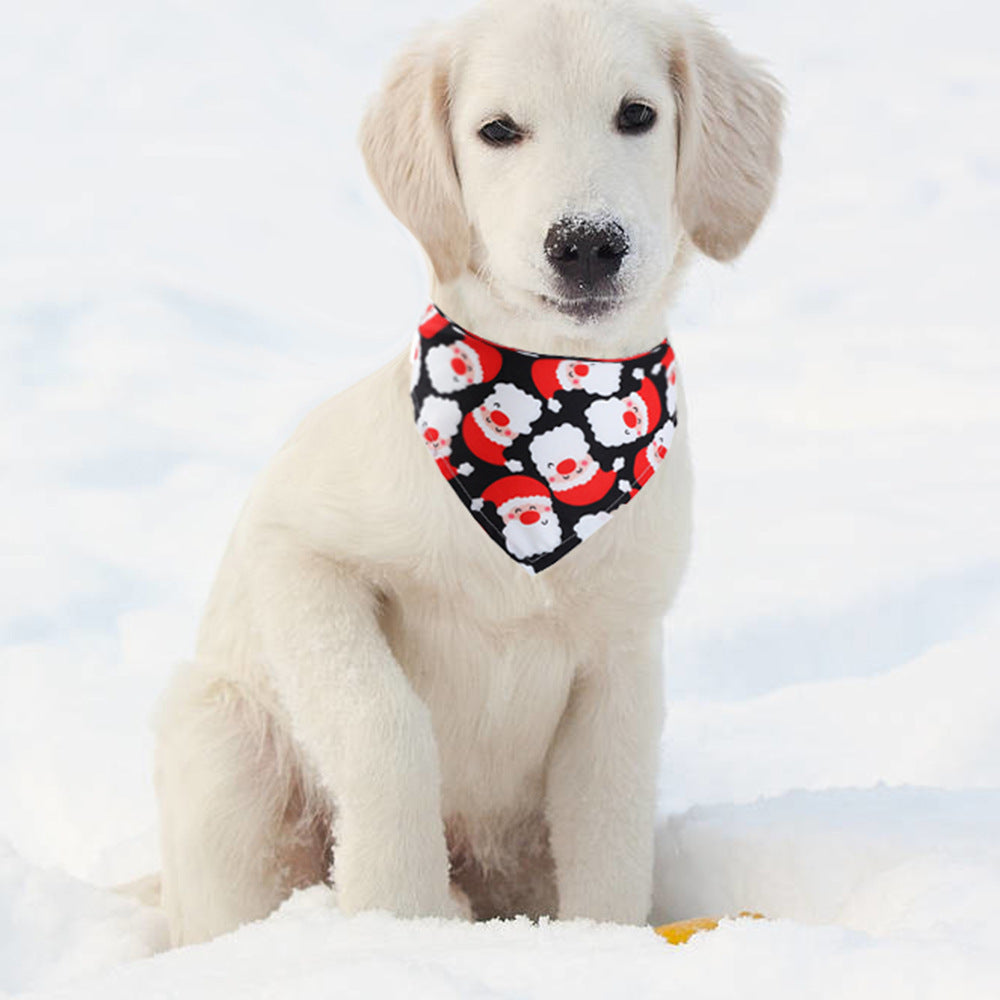 Cute white puppy wearing a Christmas dog bandana with Santa Claus faces sitting in the snow outdoors