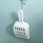 Load image into Gallery viewer, White plastic cat litter scoop hanging on a hook against a light blue wall background
