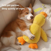 Dog cuddling with yellow squeaky duck plush toy calming chew pillow on bed