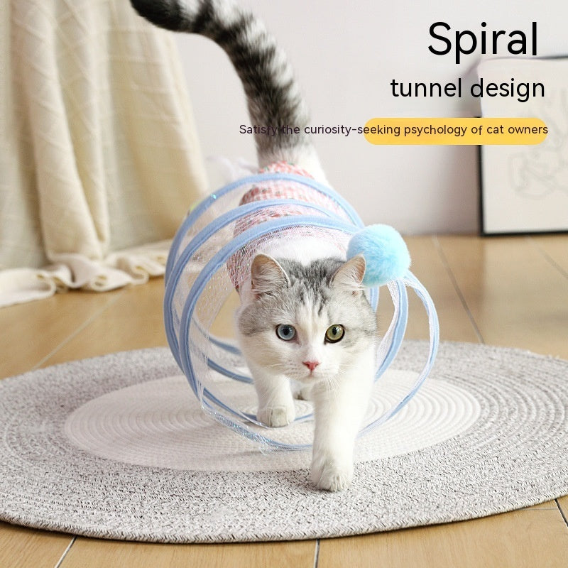 Cat playing inside a collapsible spiral tunnel toy with a blue pom-pom on a circular rug indoors