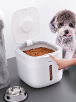Load image into Gallery viewer, White sealed pet grain storage box filled with dry food next to a small dog licking its lips and a hand opening the lid
