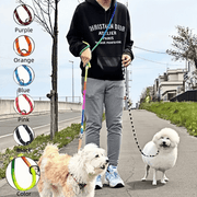 Person walking two dogs using a hands-free dog leash with shoulder strap in various colors on a paved path