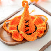 Orange knitted Halloween wizard hat with ruffled brim and black decorative stitches on wooden tray for pets