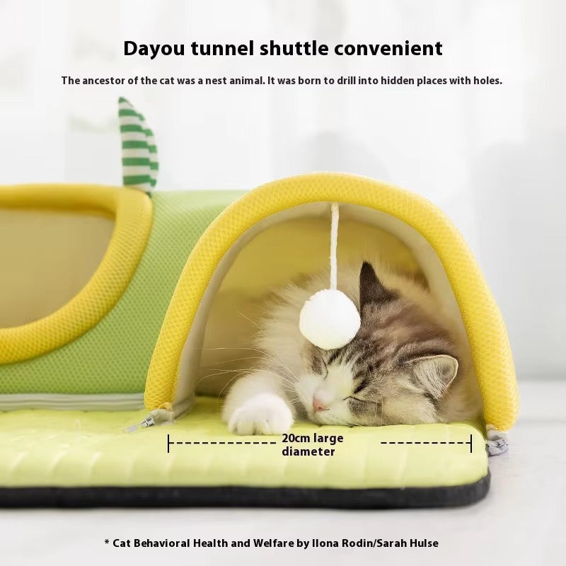 Cat sleeping inside a breathable yellow and green tunnel bed with a hanging white toy ball inside the cat tunnel bed.